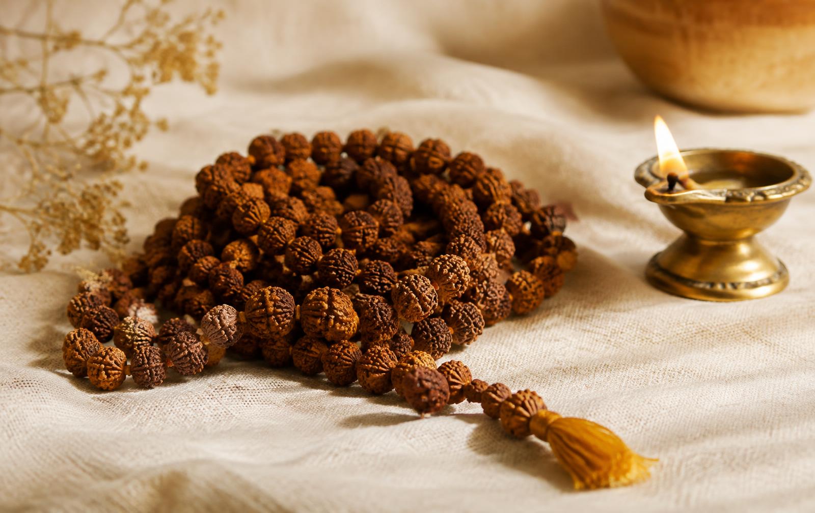 Rudraksha mala on ivory linen beside a brass oil lamp (sample photograph)